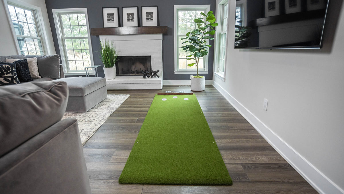 A PrimePutt putting mat rolled out across the floor of a living room, couch and fireplace behind it